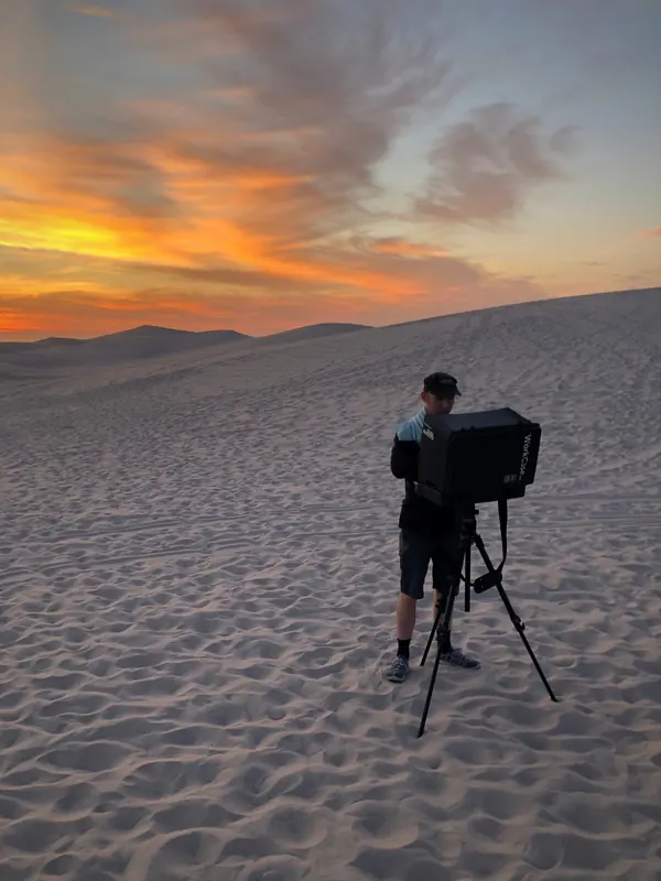 Christoph Hagen with a camera on a tripod in the dunes at sunset